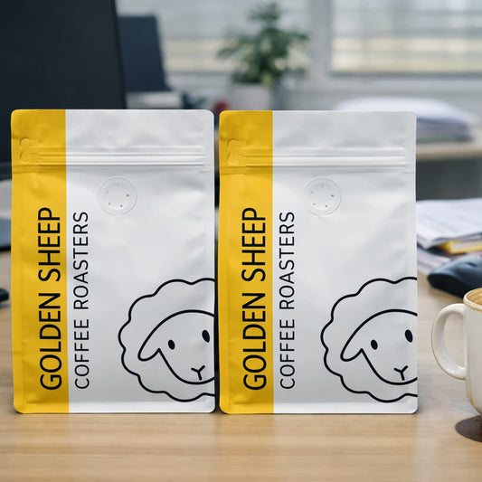Two packages of Golden Sheep Coffee Roasters on a desk with a coffee cup.