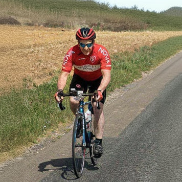 Cyclist in a red jersey riding on a road with a field in the background