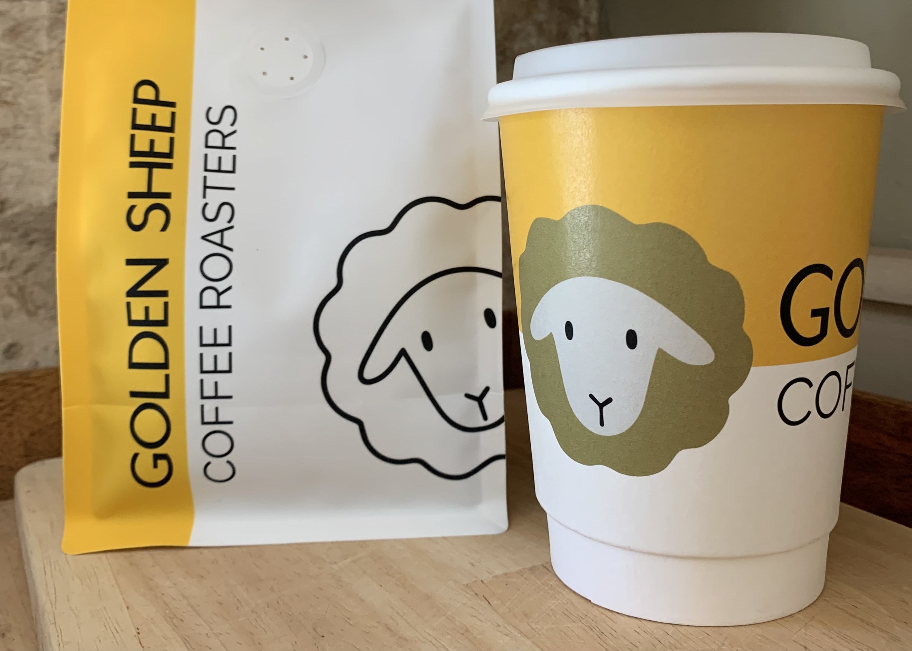 Golden Sheep Coffee Roasters coffee bag and cup on a wooden surface.
