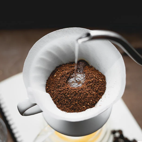 Coffee grounds being poured into a white coffee filter with a dark background