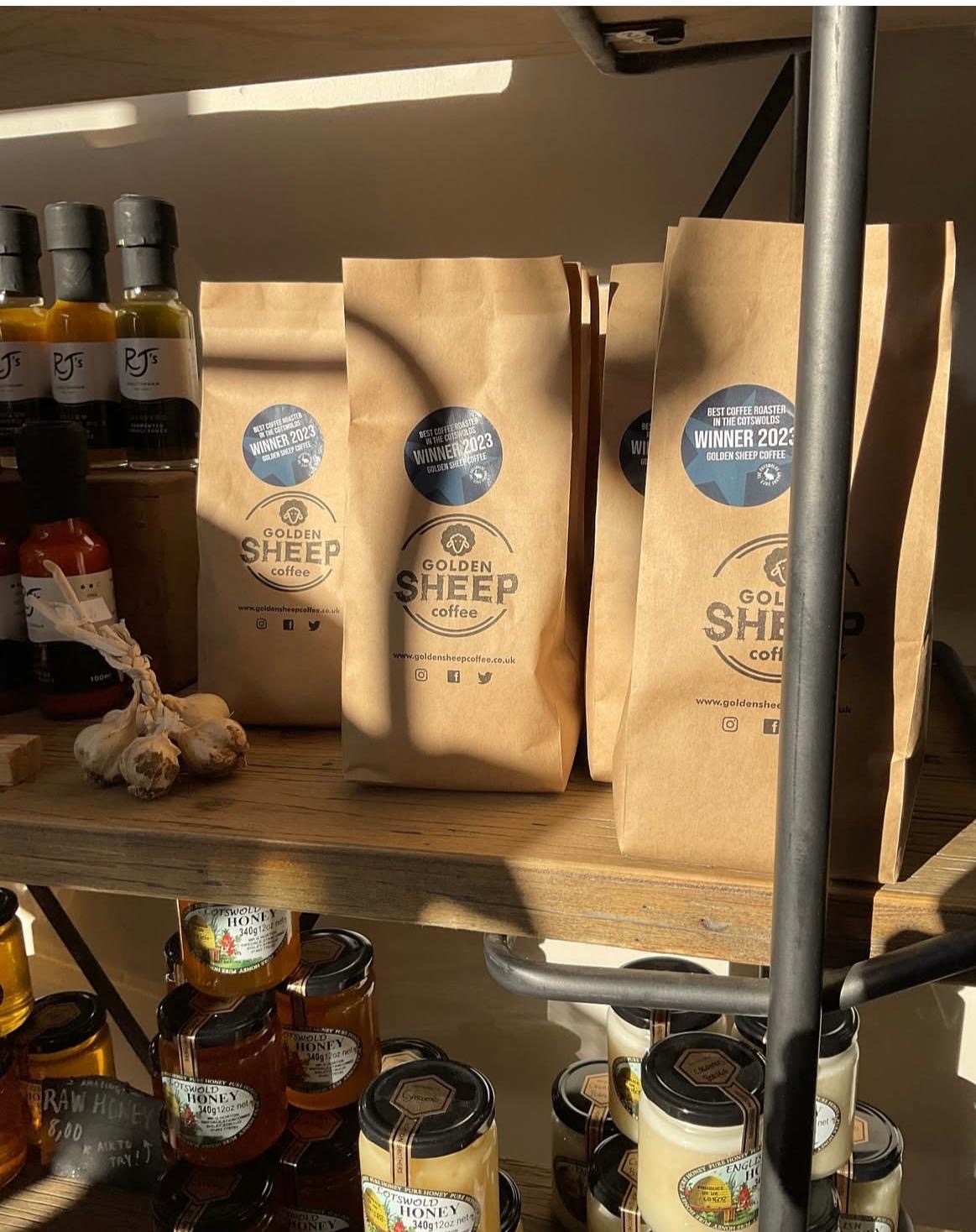 Bags of Golden Sheep coffee on a wooden shelf with various products around.