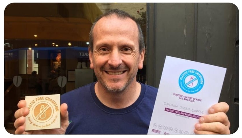 Michael holding a certificate and a gold card in front of a building entrance.