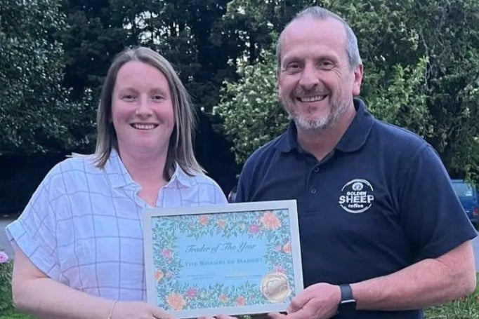 Libbie and Michael holding a framed certificate outdoors with greenery in the background